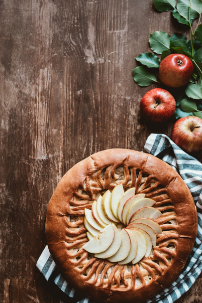 top view of arranged apple pie and fresh apples with green leaves on wooden surface - Photo, Image