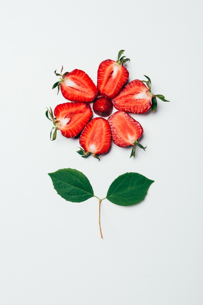 top view of flower made of sliced strawberries and green leaves on white - Photo, Image