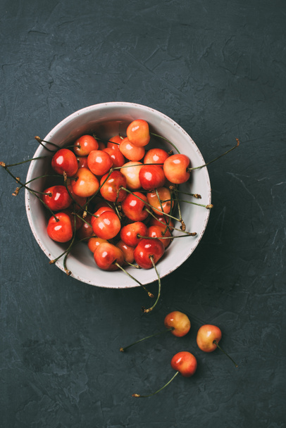 top view of fresh ripe sweet cherries in bowl on black - 写真・画像