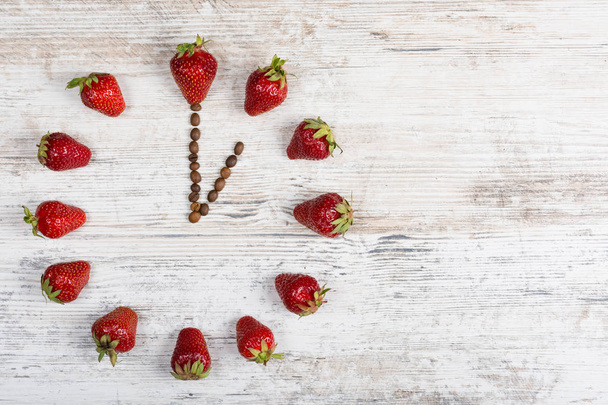 Erdbeeruhr mit Pfeilen aus Kaffeebohnen, die die Zeit in einer Stunde oder dreizehn Stunden auf einem alten hölzernen Hintergrund in der Küche anzeigt - Foto, Bild