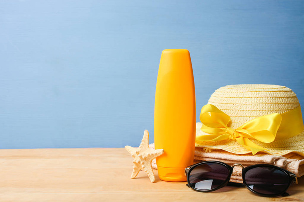 Protezione solare, cappello da spiaggia e occhiali da sole su un tavolo di legno su sfondo blu
. - Foto, immagini