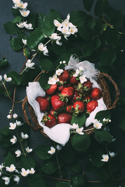 top view of beautiful jasmine flowers and sweet ripe strawberries in basket - Photo, Image