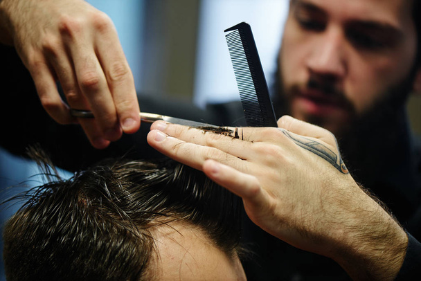 Barber man in the black shirt in the process of cutting a customer in the barbershop - Фото, зображення