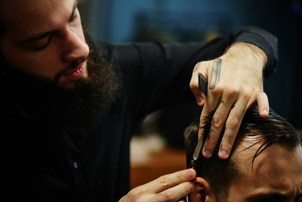 Barber man in the black shirt in the process of cutting a customer in the barbershop - Foto, Bild