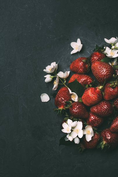 top view of ripe red strawberries and jasmine flowers on black  - Fotoğraf, Görsel