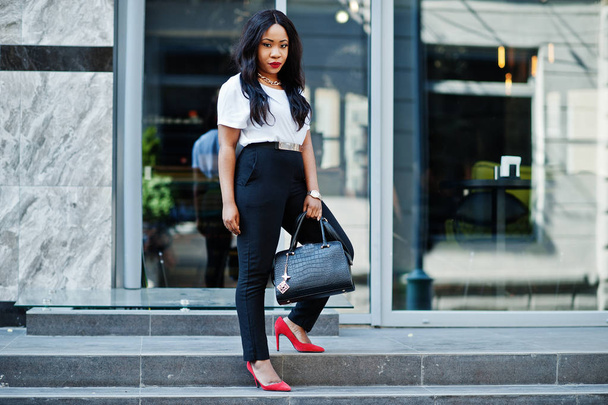 Stylish african american business woman with handbag on streets of city. - Фото, изображение