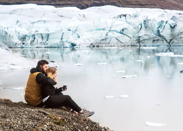 two tourists are sitting near the glacier iceberg in Iceland - Photo, image