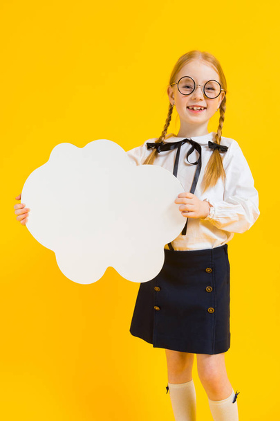 Mädchen mit roten Zöpfen auf gelbem Hintergrund. ein charmantes Mädchen mit runder durchsichtiger Brille hält eine weiße Wolke in ihren Händen. - Foto, Bild