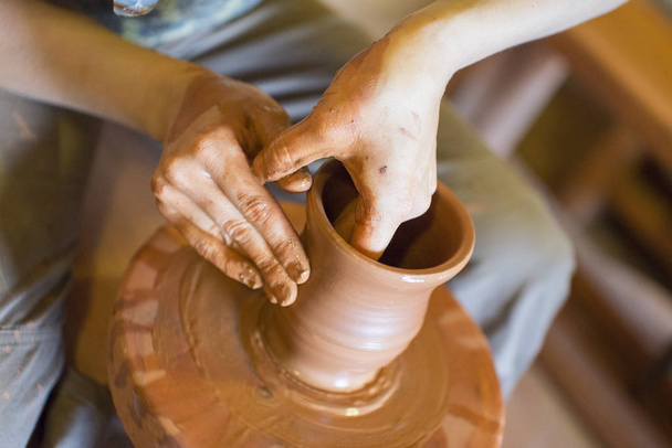 それをホイールと粘土陶器の花瓶を陶工回転: 上から撮影しました。粘土の手。陶芸: 男性陶芸家手作り粘土製品を作成します。陶芸家のホイール、陶芸家の手の回転のプロセス. - 写真・画像