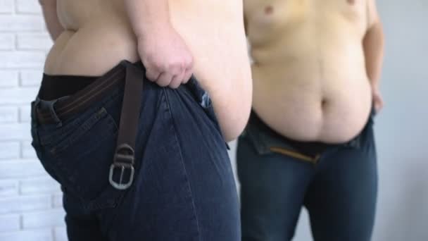 Ожирний чоловік одягає джинси з зусиллями перед дзеркалом, здоров'ям, невпевненістю
 - Кадри, відео
