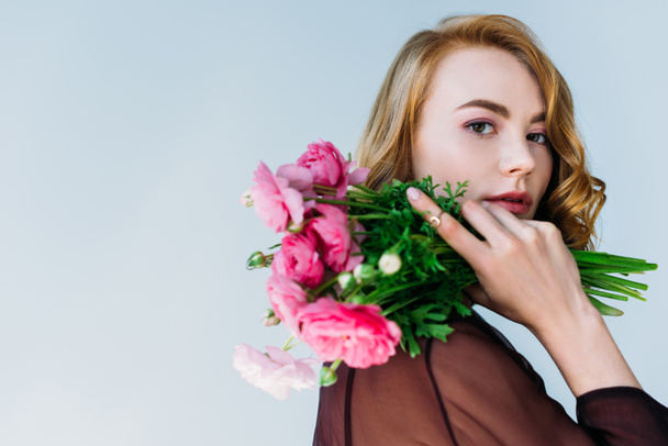beautiful young woman holding tender flowers and looking at camera isolated on grey - Foto, afbeelding