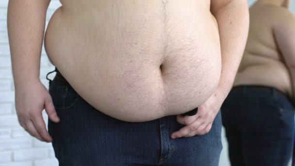 Oversize man holding fat stomach while tightening jeans belt, metabolic disorder - Footage, Video