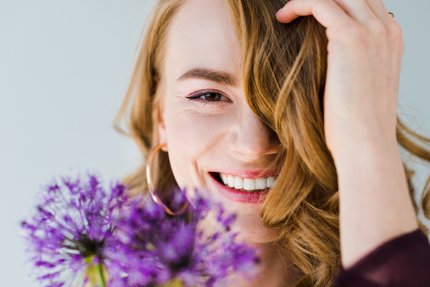 beautiful girl holding fresh violet flowers and smiling at camera isolated on grey - Photo, image
