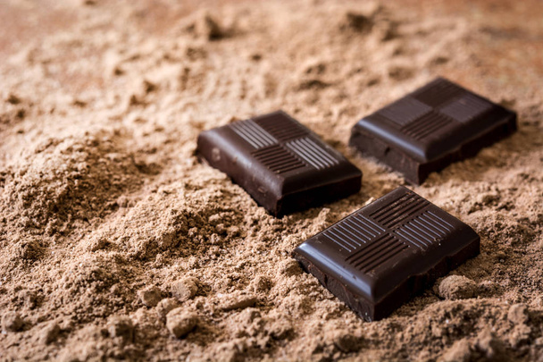 Κομμάτια σοκολάτας σε σκόνη σοκολάτας. Copyspace - Φωτογραφία, εικόνα