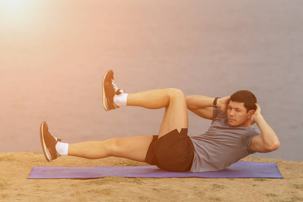 siedzieć ups - człowiek fitness ćwiczenia siedzieć się na zewnątrz w trawie w okresie letnim. dopasowanie sportowcem pracy Krzyż szkolenia w okresie letnim. kaukaski mięśni sportowy model w jego 20s. - Zdjęcie, obraz