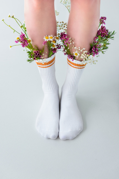 γκρο πλαν μερική άποψη της γυναικεία πόδια σε κάλτσες με όμορφα λουλούδια που απομονώνονται σε γκρι  - Φωτογραφία, εικόνα