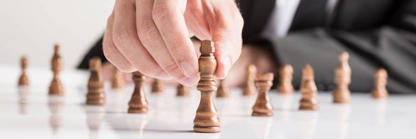 Wide cropped image of businessman wearing business suit moving dark King chess piece at white table. - Photo, Image
