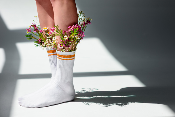 cropped shot of young woman with beautiful flowers in socks standing on grey  - Photo, Image