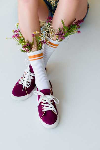cropped shot of young woman with flowers in socks sitting isolated on grey - 写真・画像