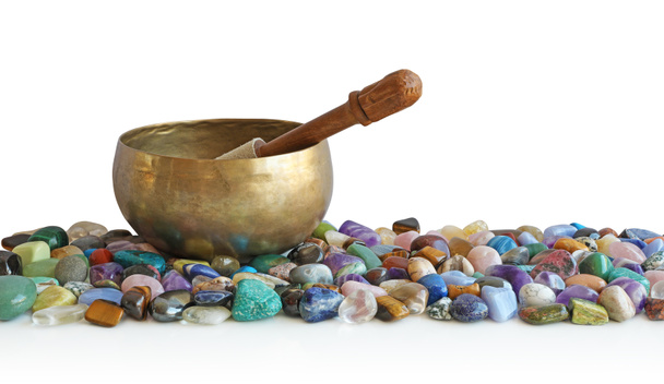 Singing bowl resting on bed of tumbled healing stones - a tibetan singing bowl atop a neat selection of multicoloured healing chakra stones against a white background - Photo, Image