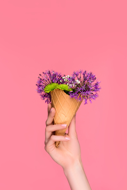 close-up partial view of female hand holding waffle cone with beautiful flowers isolated on pink - Фото, изображение