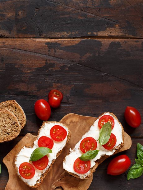 Bruschetta z twarogiem, pomidorkami i bazylia na drewnianym stole - Zdjęcie, obraz