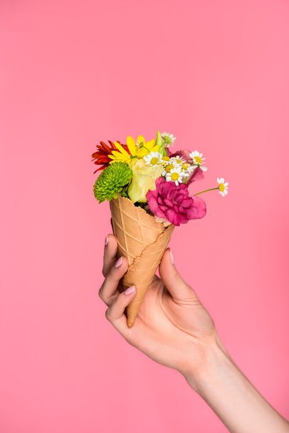close-up partial view of woman holding ice cream cone with beautiful flowers isolated on pink - Foto, Bild
