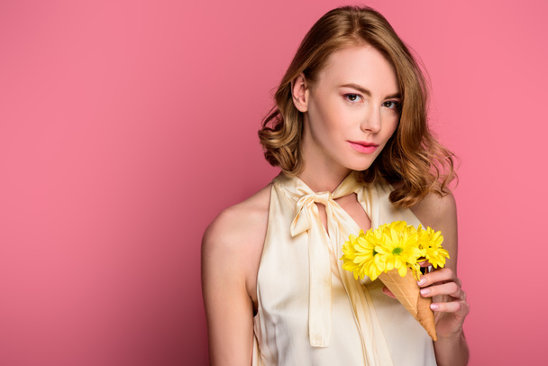 Dziewczyna trzyma stożek lody z żółtych kwiatów i patrząc na kamery na różowym tle - Zdjęcie, obraz