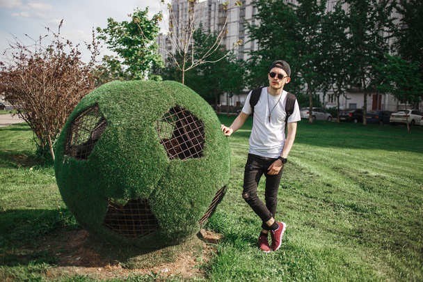 Stylish handsome man tourist posing near soccer ball symbol of grass. Russian World cup concept. - Zdjęcie, obraz