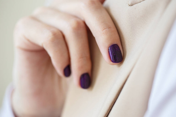 Gorgeous manicure, dark purple tender color nail polish, closeup photo. Female hands over simple background of casual clothes - 写真・画像
