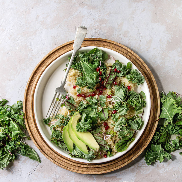 Vegan quinoa salad with kale, young beetroot leaves, garnet seeds, sliced avocado in white plate with ingredients above over grey texture background. Top view, space. Healthy eating - Fotografie, Obrázek