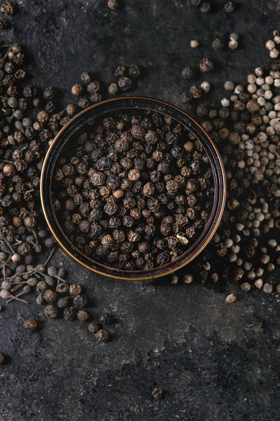 Variety of different black peppers allspice, pimento, monks pepper, peppercorns in tin can over old black iron texture background. Top view, copy space. - Zdjęcie, obraz