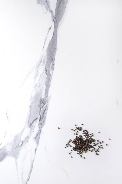 Heap of black pepper peppercorns over white marble texture background. Top view, space. - Fotoğraf, Görsel