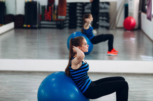 Jonge vrouw zitten op een pilates bal in sportschool - Foto, afbeelding