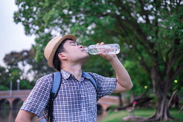 azjatycki człowiek młody wiek 25-30 roku turystów backpacker. on był spragniony i wody pitnej z plastikowej butelki. podczas podróży wakacje i relaks. - Zdjęcie, obraz