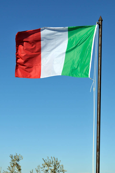 Tricolor italiano, bandeira da Itália, acenando com fundo céu azul ensolarado
 - Foto, Imagem