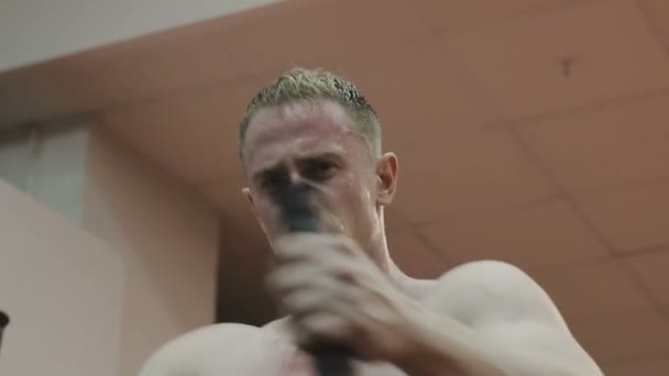 A muscular man with a naked torso trains on a fitness machine in a fitness club - Materiał filmowy, wideo