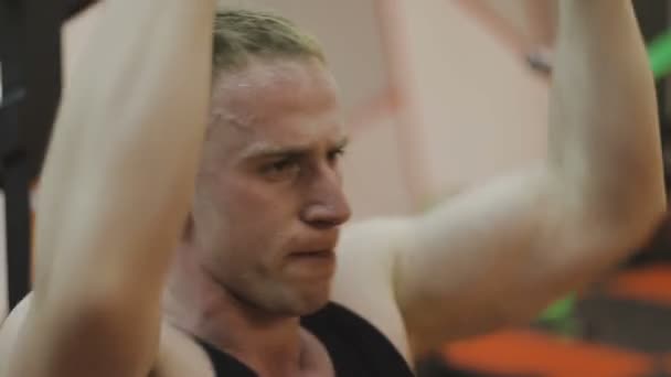 A muscular man in a black T-shirt is training on a fitness machine in a fitness club. - Video