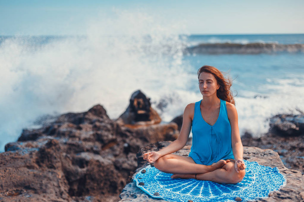 Молодая женщина, практикующая йогу на скале, медитирует в позе лотоса
. - Фото, изображение