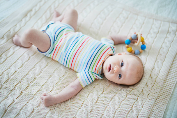Adorable baby girl lying on bed in nursery and playing with teething toy - Photo, Image