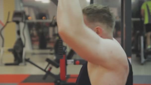 A muscular man in a black T-shirt is training on a fitness machine in a fitness club. - Filmmaterial, Video
