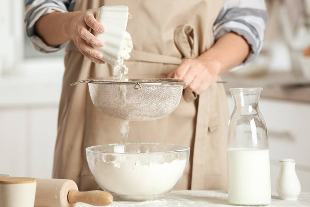 Woman sifting flour into bowl on table in kitchen - Φωτογραφία, εικόνα