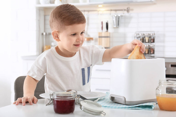 Netter kleiner Junge bereitet Toast mit süßer Marmelade am Tisch zu - Foto, Bild