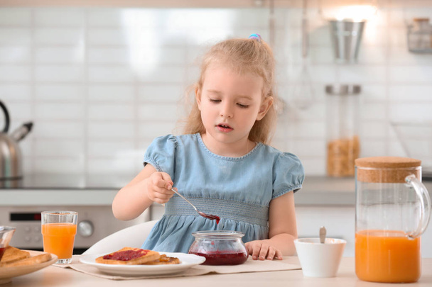 Cute little girl with tasty toasted bread and jam at table in kitchen - Фото, изображение