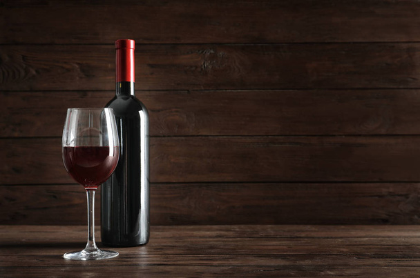 Glass and bottle with delicious red wine on table against dark background - Фото, изображение