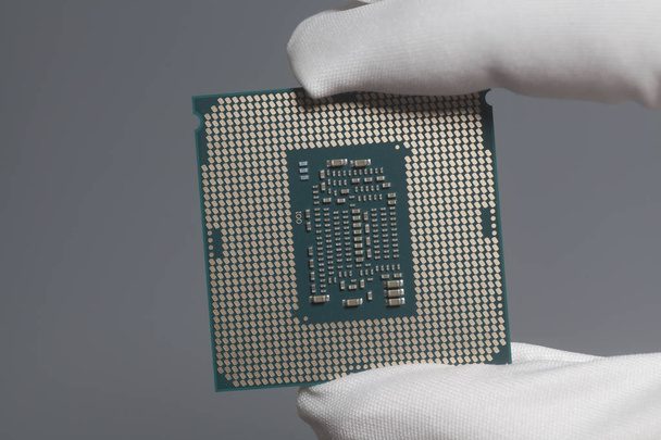 Hand in white glove holding a CPU computer processor microchip on gray - Photo, image