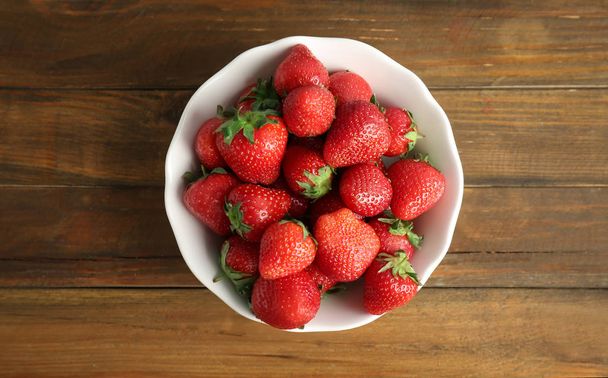 Bowl with ripe red strawberries on wooden background, top view - 写真・画像
