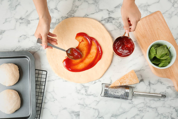 Woman spreading tomato sauce on pizza on table, top view - Photo, image