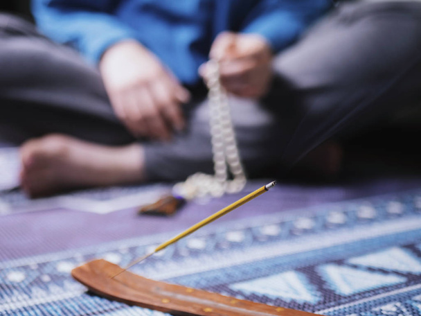 Concentrated woman praying with wooden rosary mala beads. Close up, focus on incense stick - Foto, afbeelding