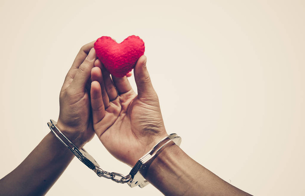 A couple' hands holding as a red heart together with hand cuffs / Love and romance on Valentine's day concept - Fotografie, Obrázek